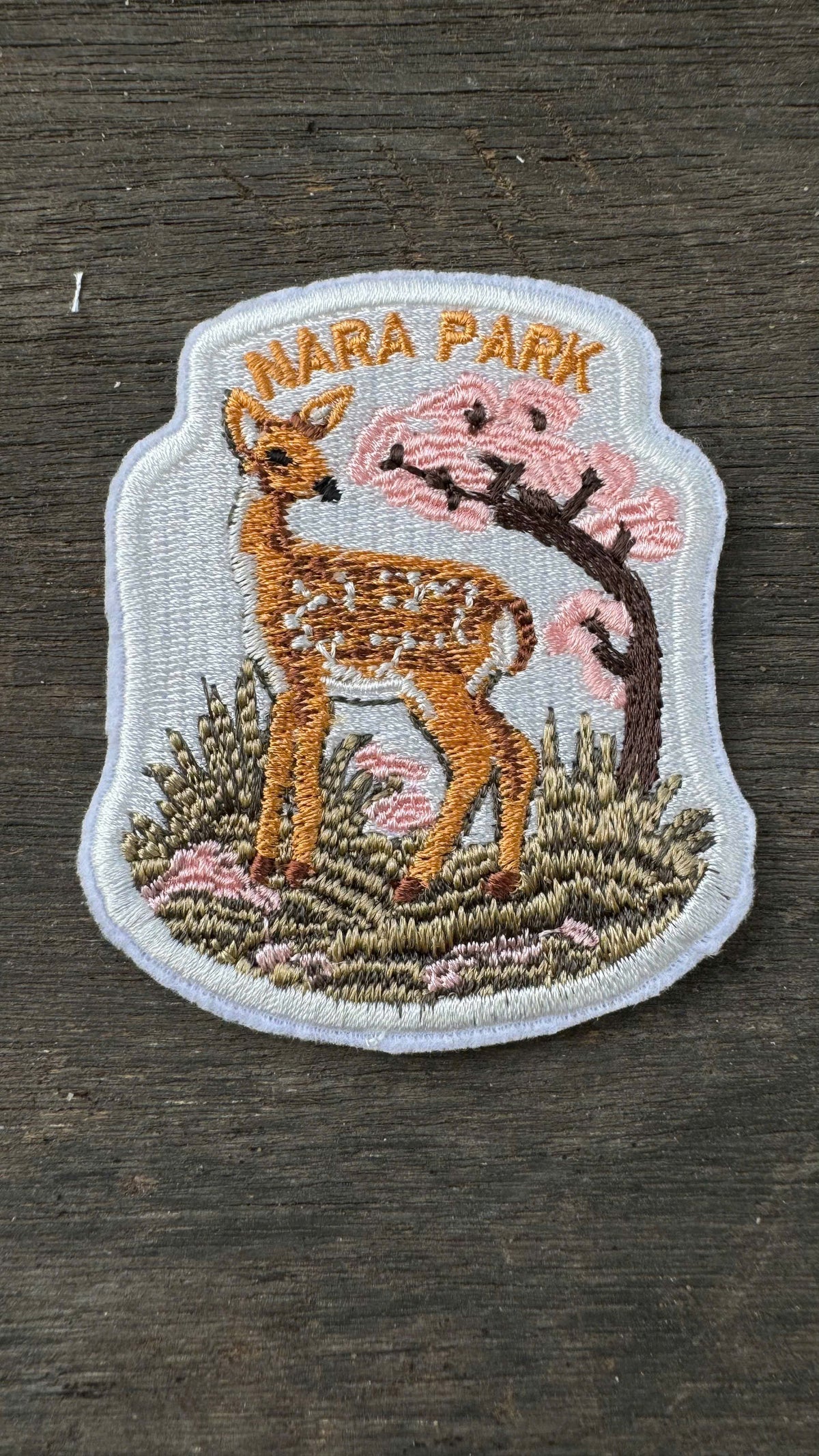Embroidered patch of a deer and cherry blossom tree with 'Nara Park' text on a wooden surface.