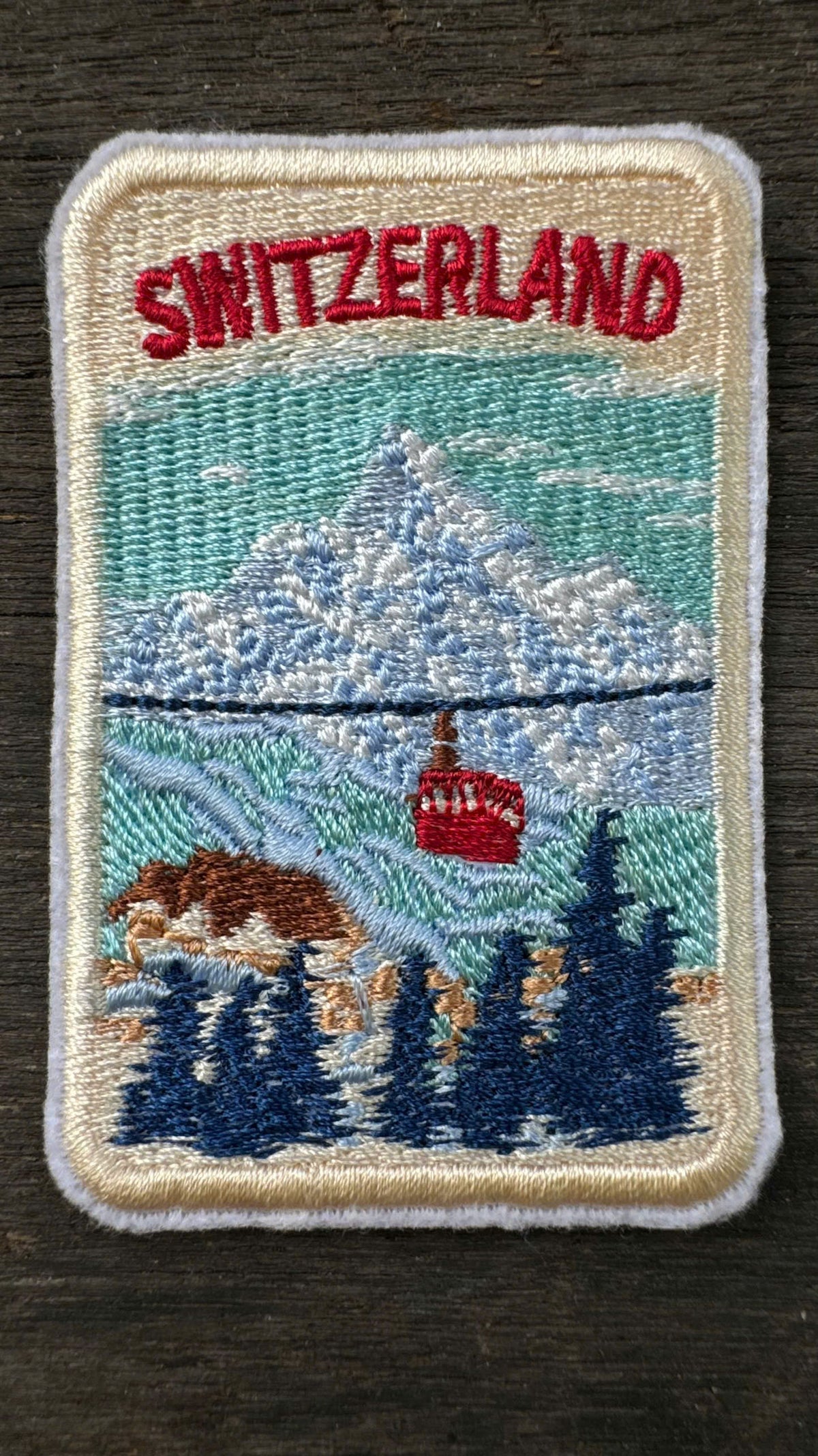Embroidered patch of Switzerland with a mountain and cable car design on a dark surface.
