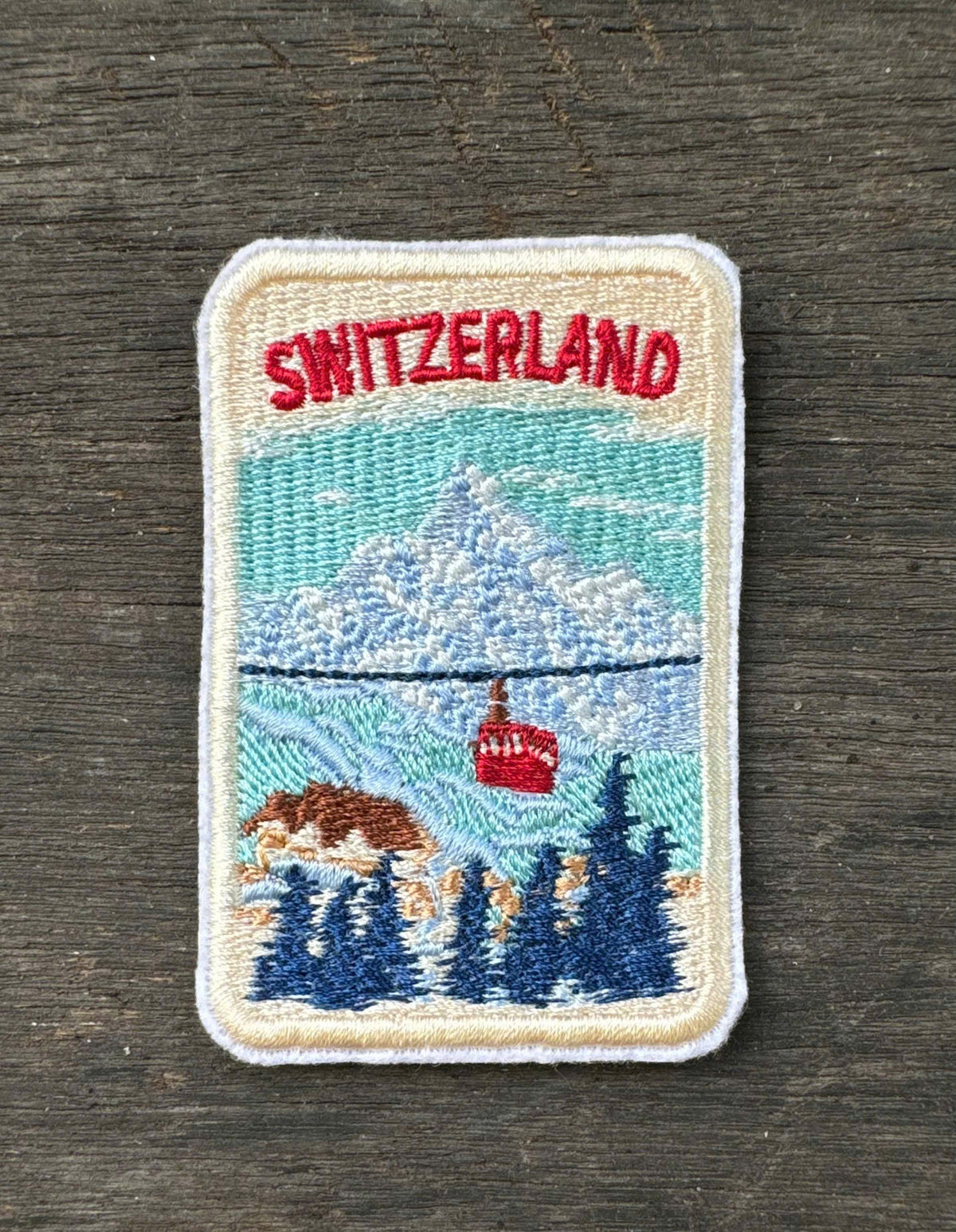 Embroidered patch of Switzerland with mountain and cable car design on a wooden surface