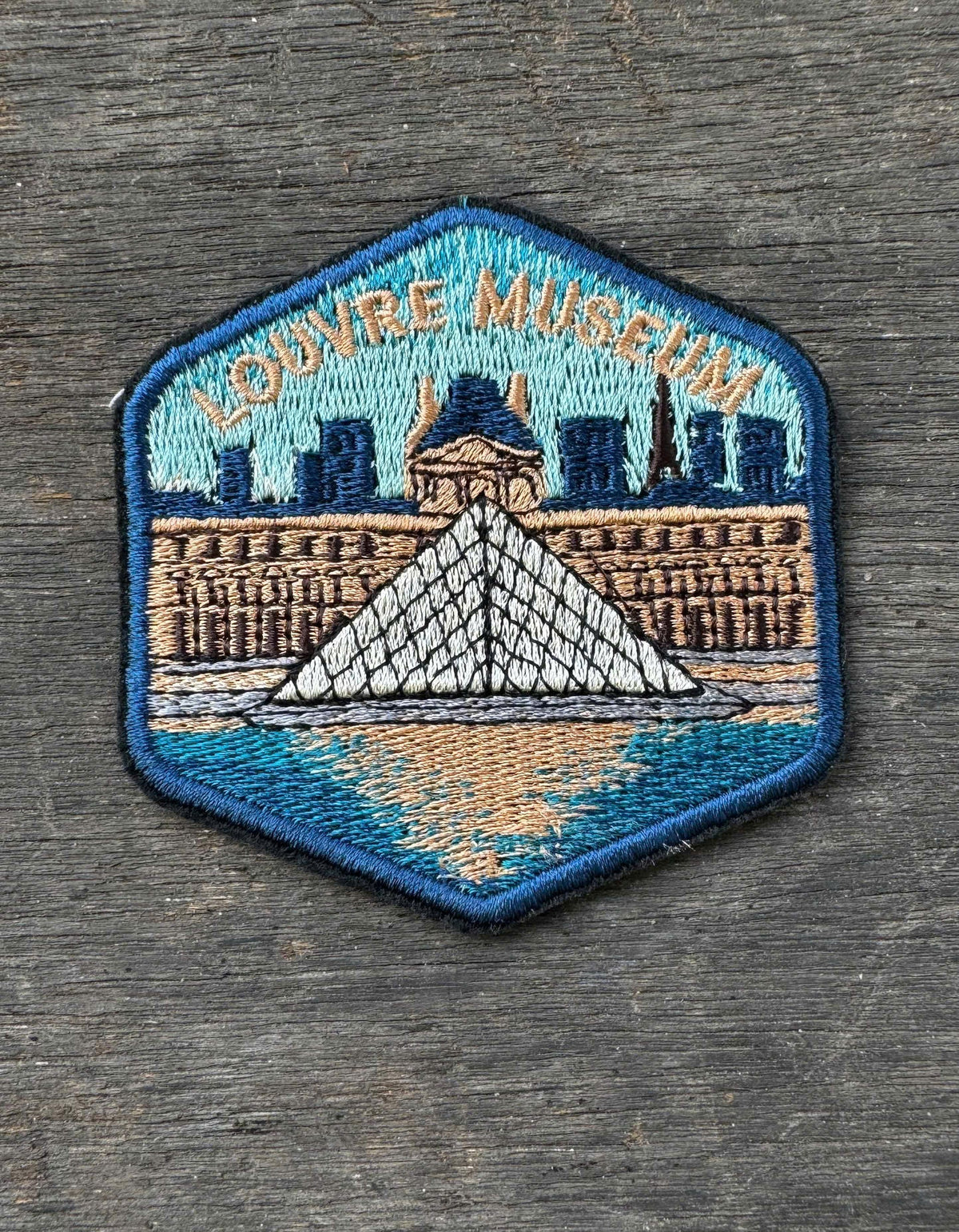 Embroidered patch of the Louvre Museum on a wooden surface