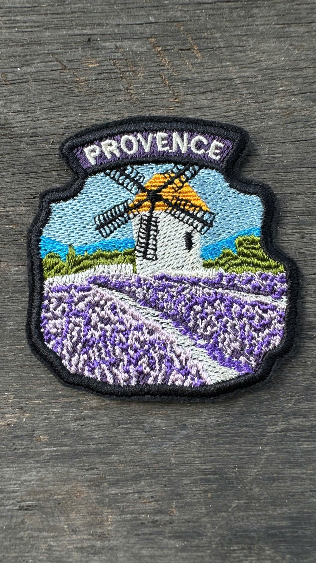 Embroidered patch with a windmill and lavender field design, labeled 'Provence', on a wooden surface.