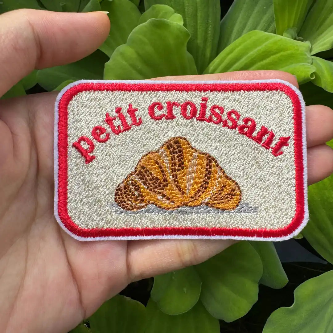 Cute croissant patch with red text and white background"
