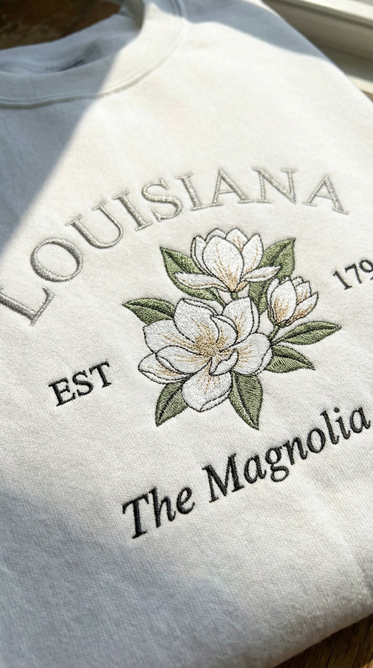 White sweatshirt with embroidered design of magnolias and text on a light background