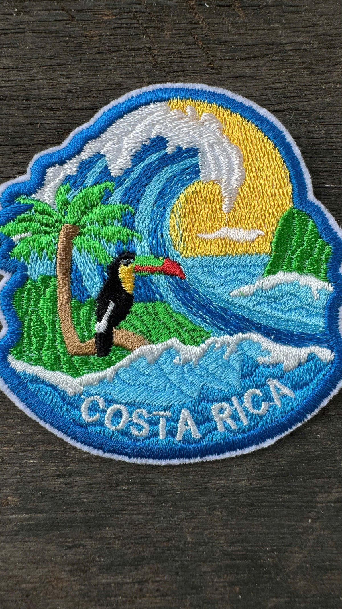 Embroidered patch of Costa Rica with a toucan, palm tree, and wave on a dark surface