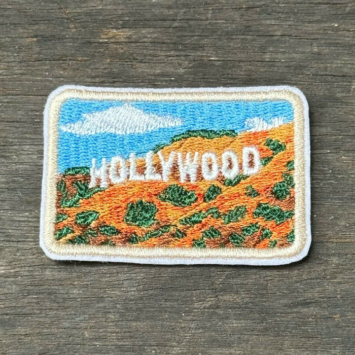 An embroidered rectangular patch depicting the Hollywood hills with the Hollywood sign, placed on a dark wood surface.