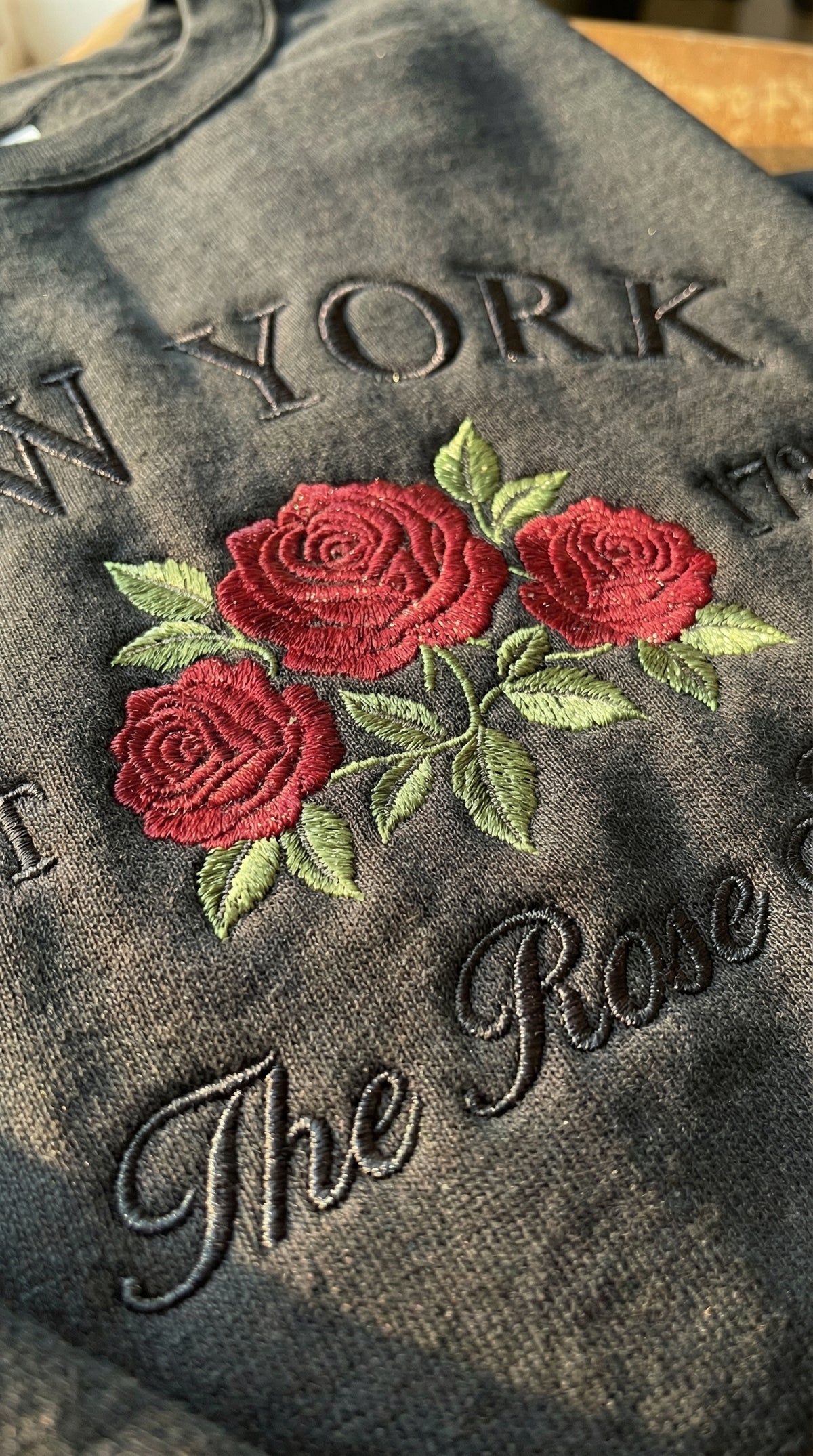 Black folded sweatshirt with detailed red Rose flower embroidery reading New York EST 1788 The Rose State