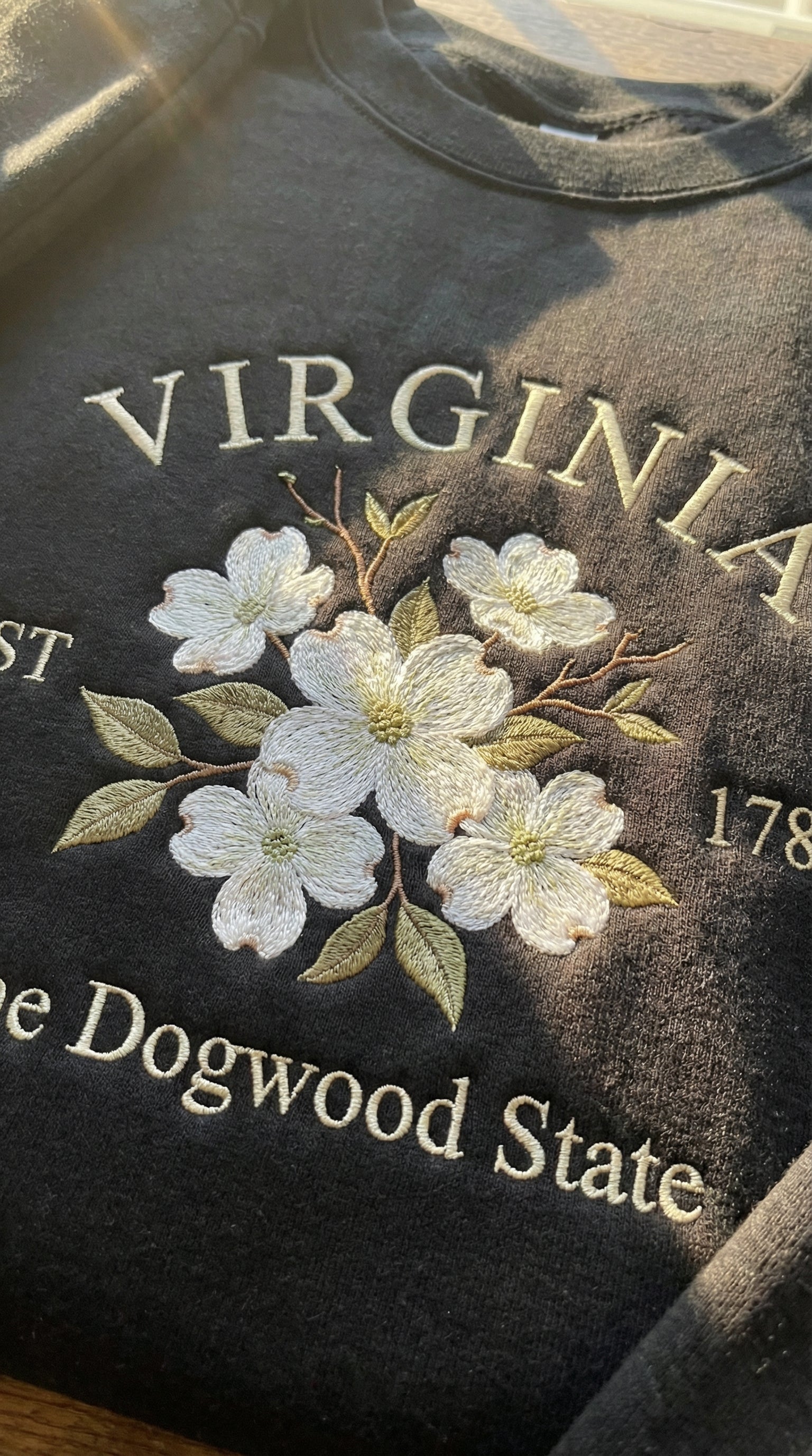 Black folded sweatshirt with detailed white Dogwood flower embroidery reading Virginia EST 1788 The Dogwood State