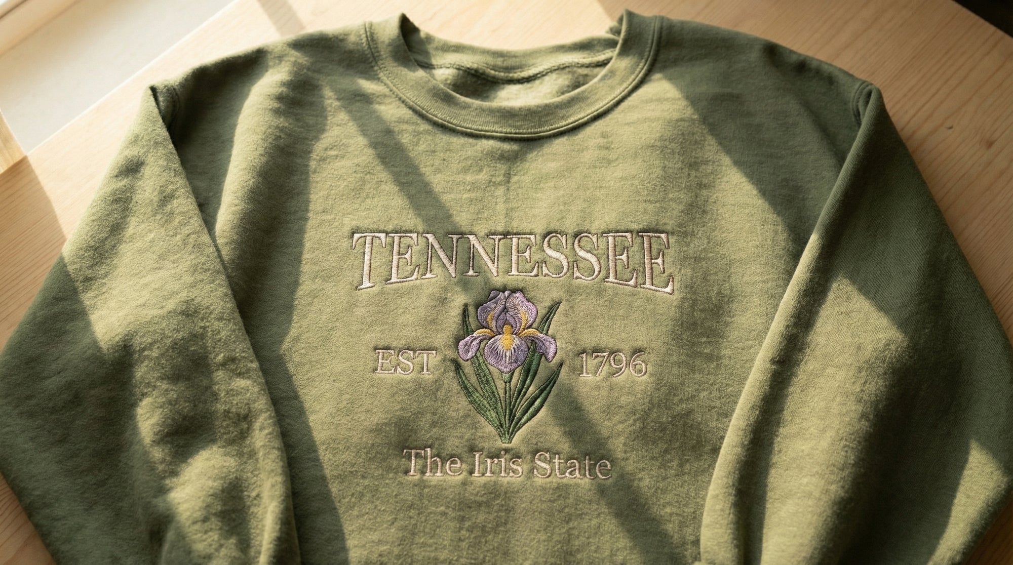 Olive green folded sweatshirt with detailed purple Iris flower embroidery reading Tennessee EST 1796 The Iris State