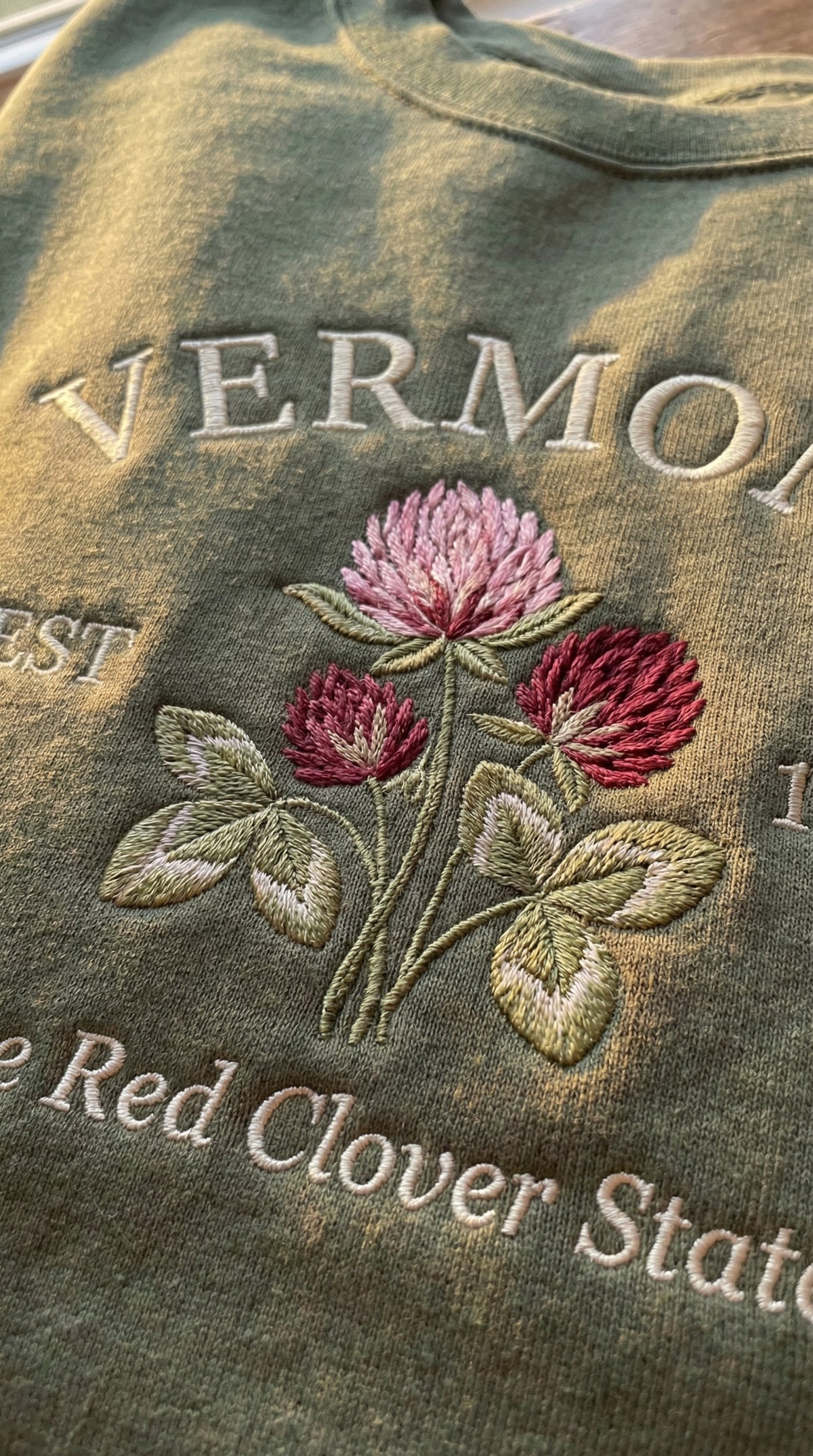 Olive green sweatshirt with detailed pink Red Clover flower embroidery, reading Vermont EST 1791 The Red Clover State