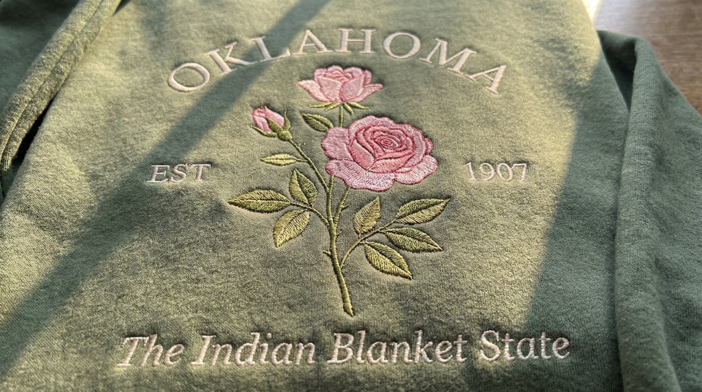 Olive green sweatshirt with detailed pink Rose flower embroidery reading Oklahoma EST 1907 The Indian Blanket State