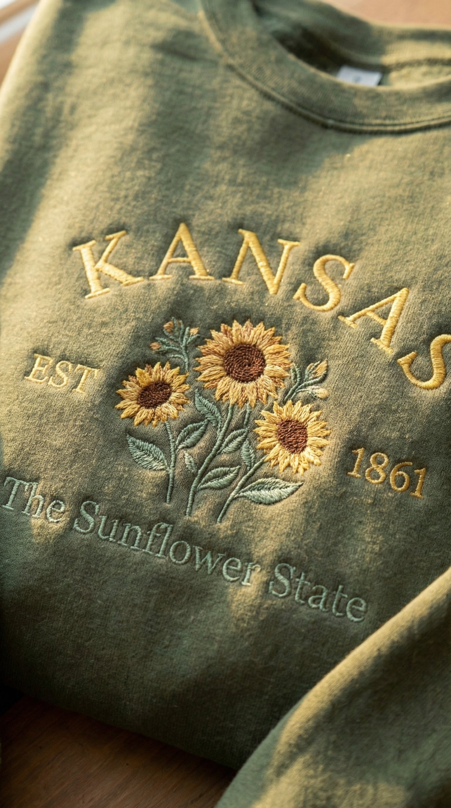 Olive green sweatshirt with detailed yellow Sunflower embroidery reading Kansas EST 1861 The Sunflower State