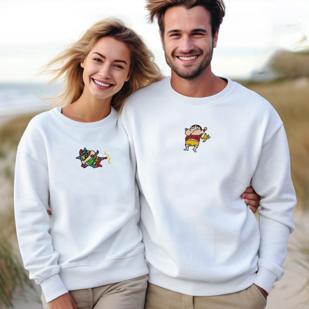 White embroidered sweatshirt with ShinChan character, couple standing outdoors by water