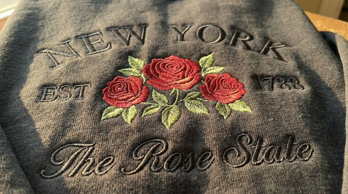 Black folded sweatshirt with detailed red Rose flower embroidery reading New York EST 1788 The Rose State