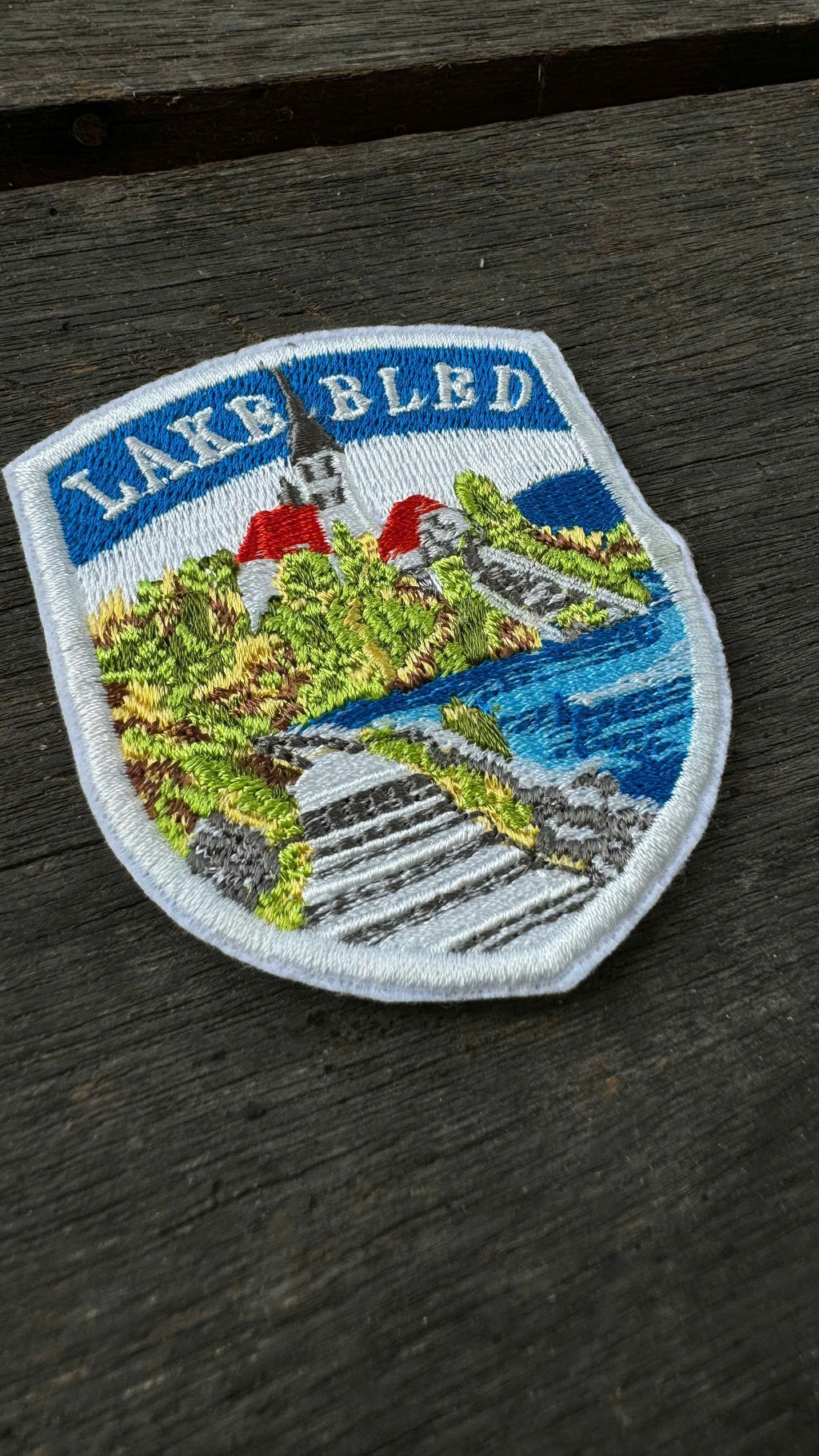 Embroidered patch of Lake Bled on a wooden surface