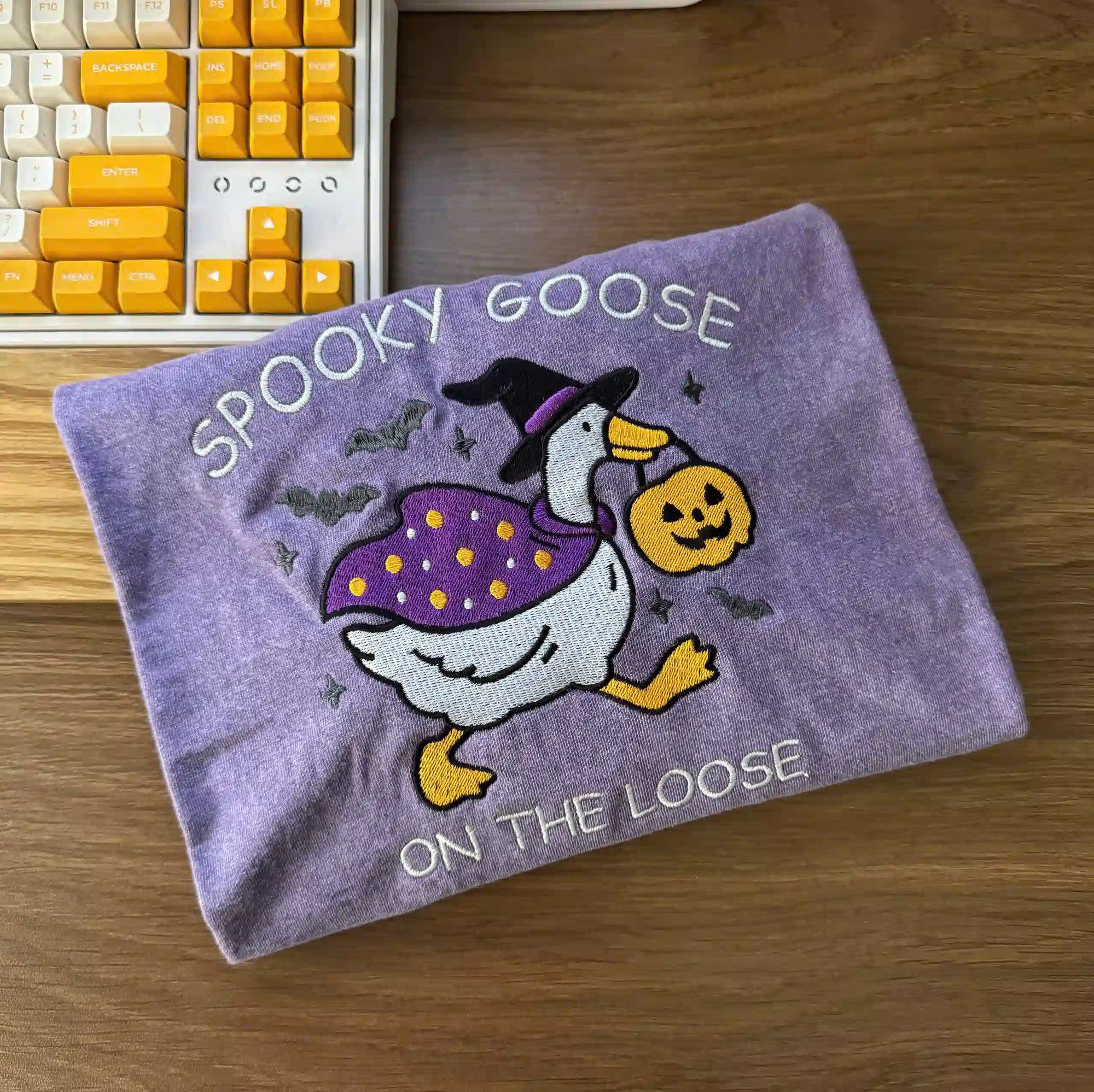 Purple towel with Halloween-themed goose design on a wooden surface next to a keyboard.