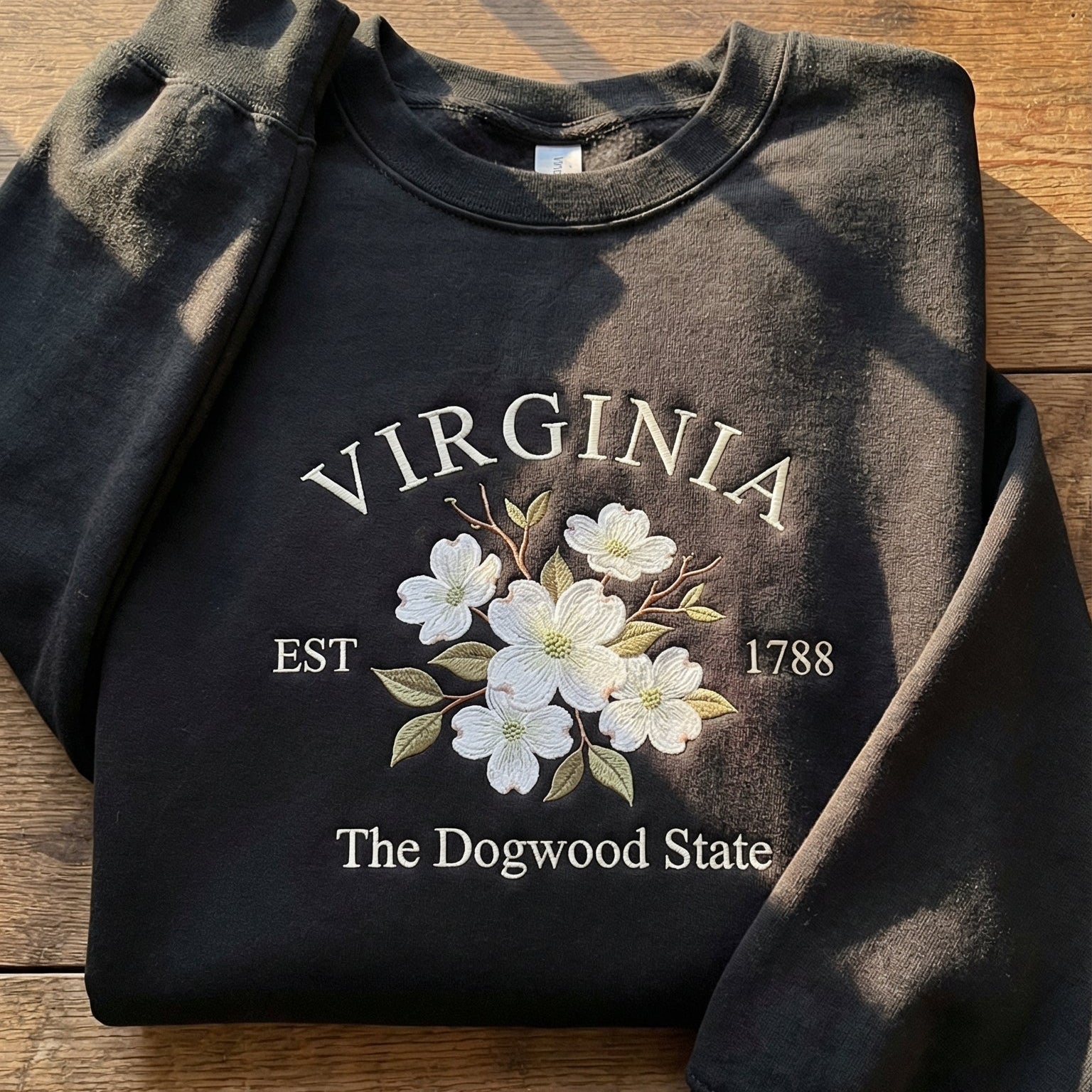 Black folded sweatshirt with detailed white Dogwood flower embroidery reading Virginia EST 1788 The Dogwood State