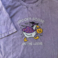 Purple t-shirt with a Halloween-themed design of a goose and text 'Spooky Goose on the Loose'.
