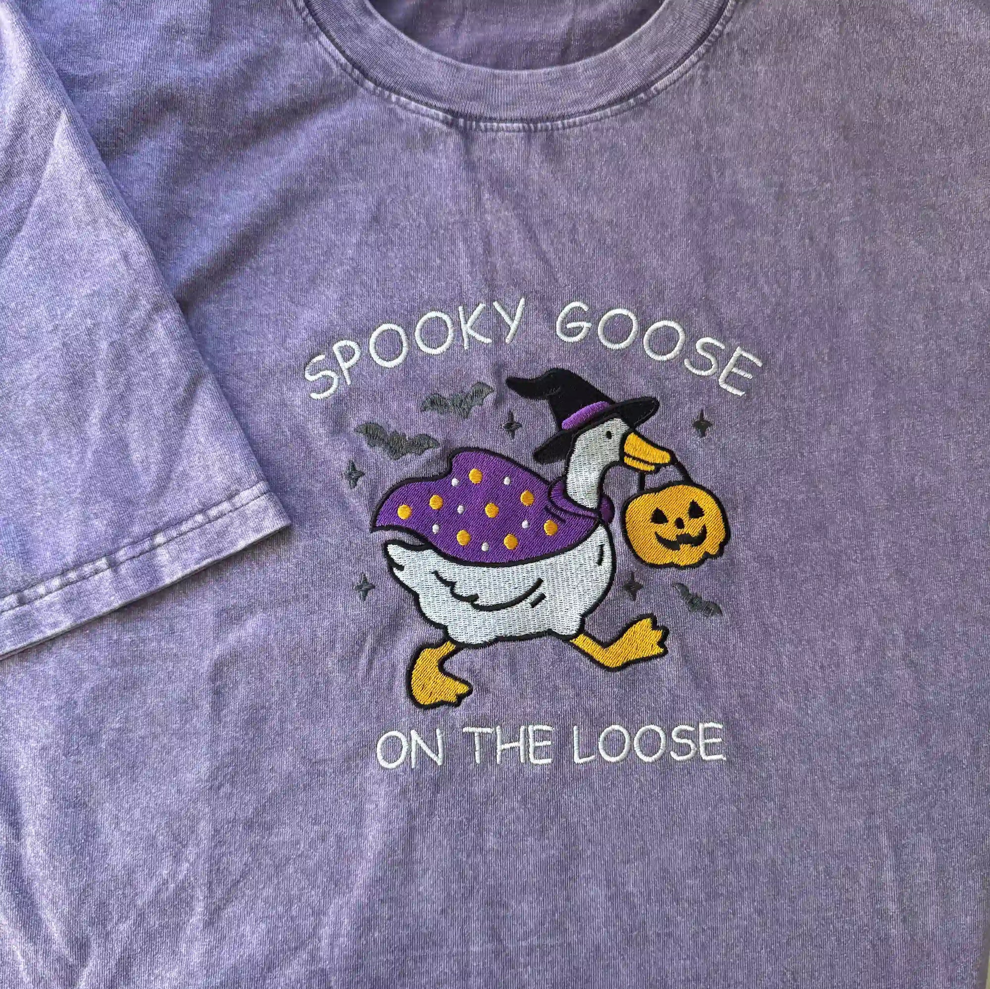 Purple t-shirt with a Halloween-themed design of a goose and text 'Spooky Goose on the Loose'.