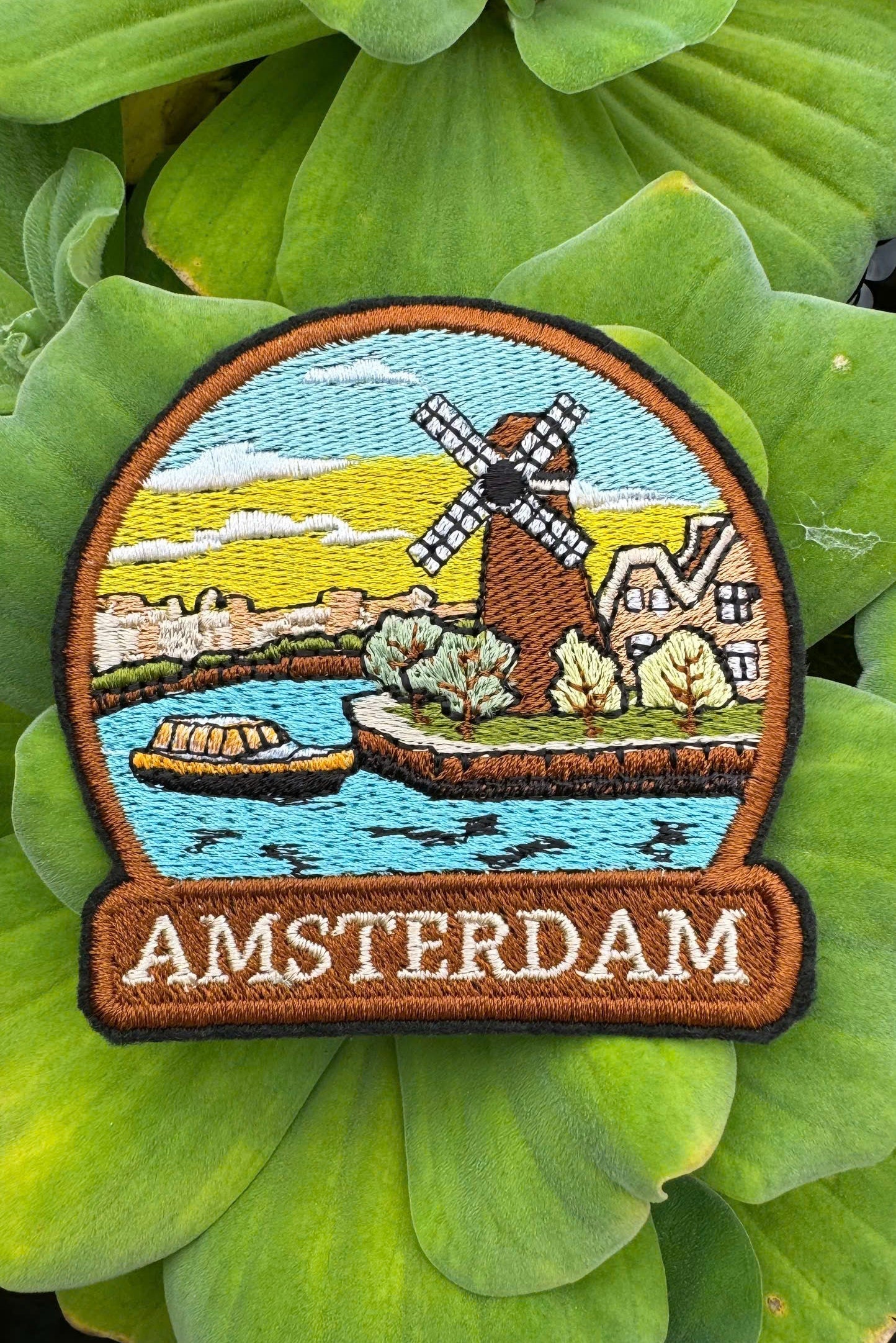 Embroidered patch of Amsterdam with a windmill design on green leaves