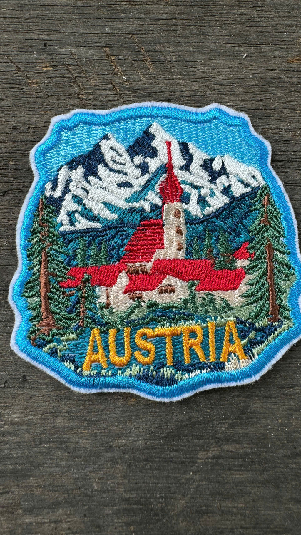 Embroidered patch of Austria with a church and mountains on a wooden surface