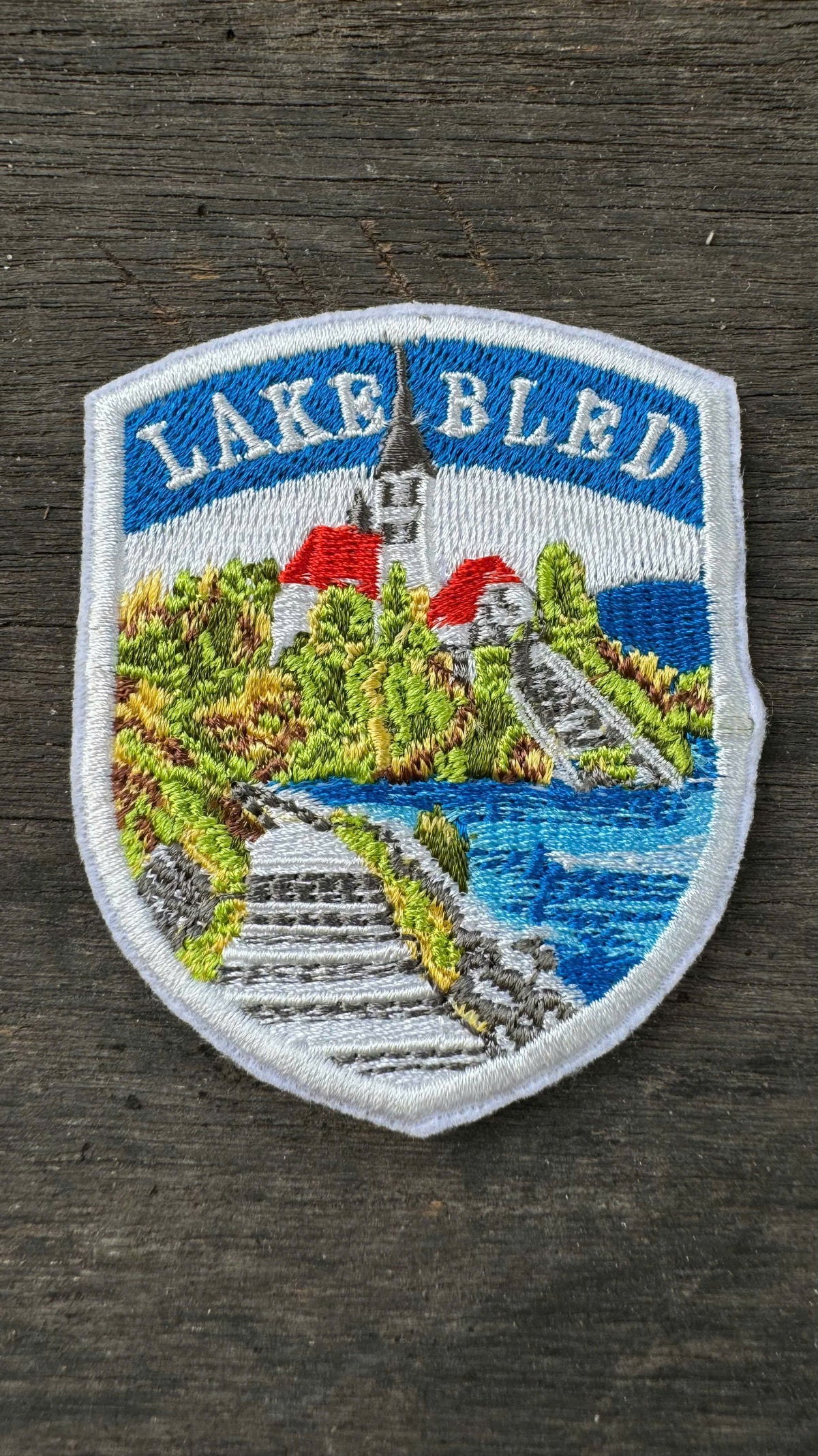 Embroidered patch of Lake Bled with scenic design on a wooden background