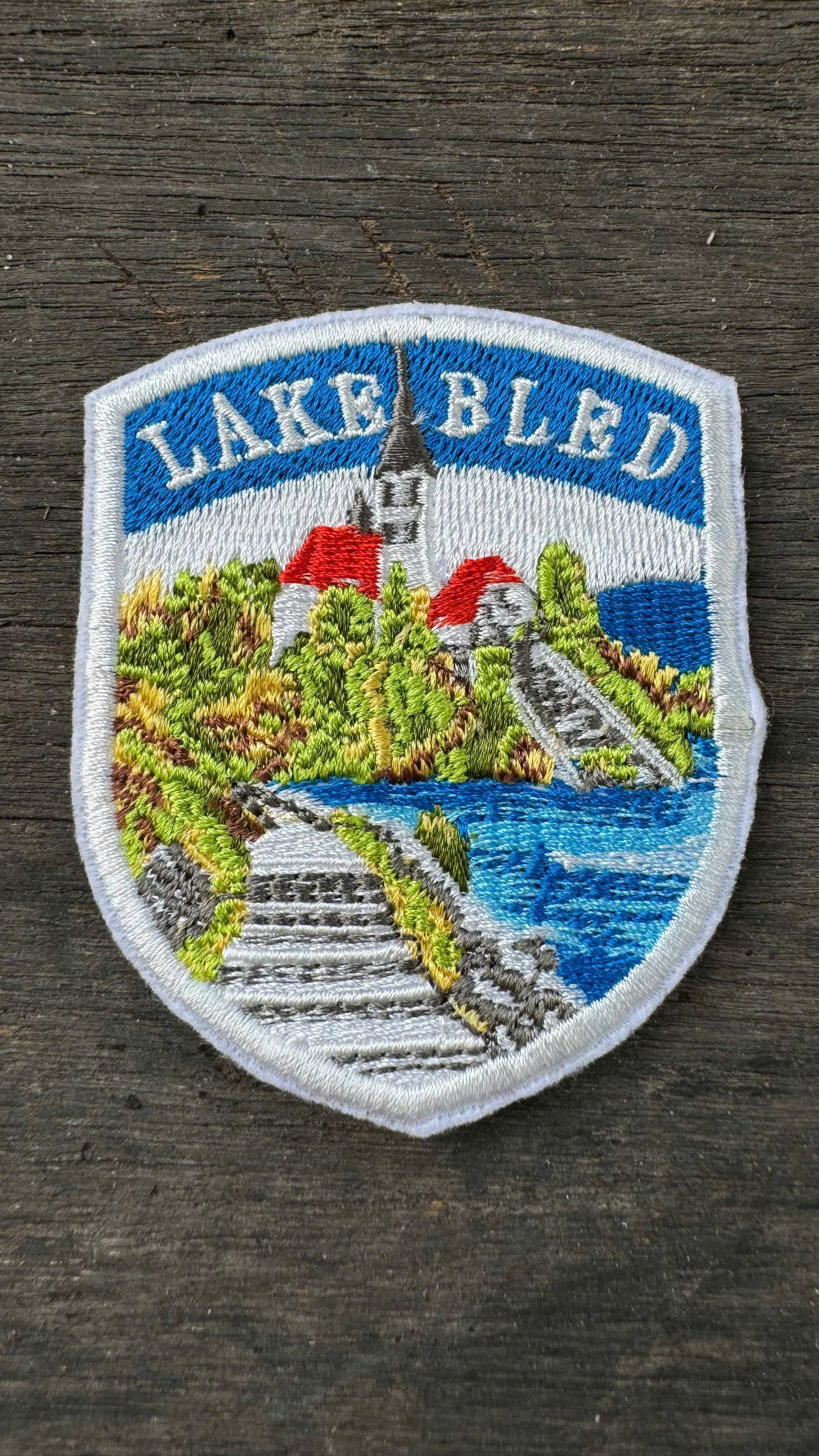 Embroidered patch of Lake Bled with scenic design on a wooden background