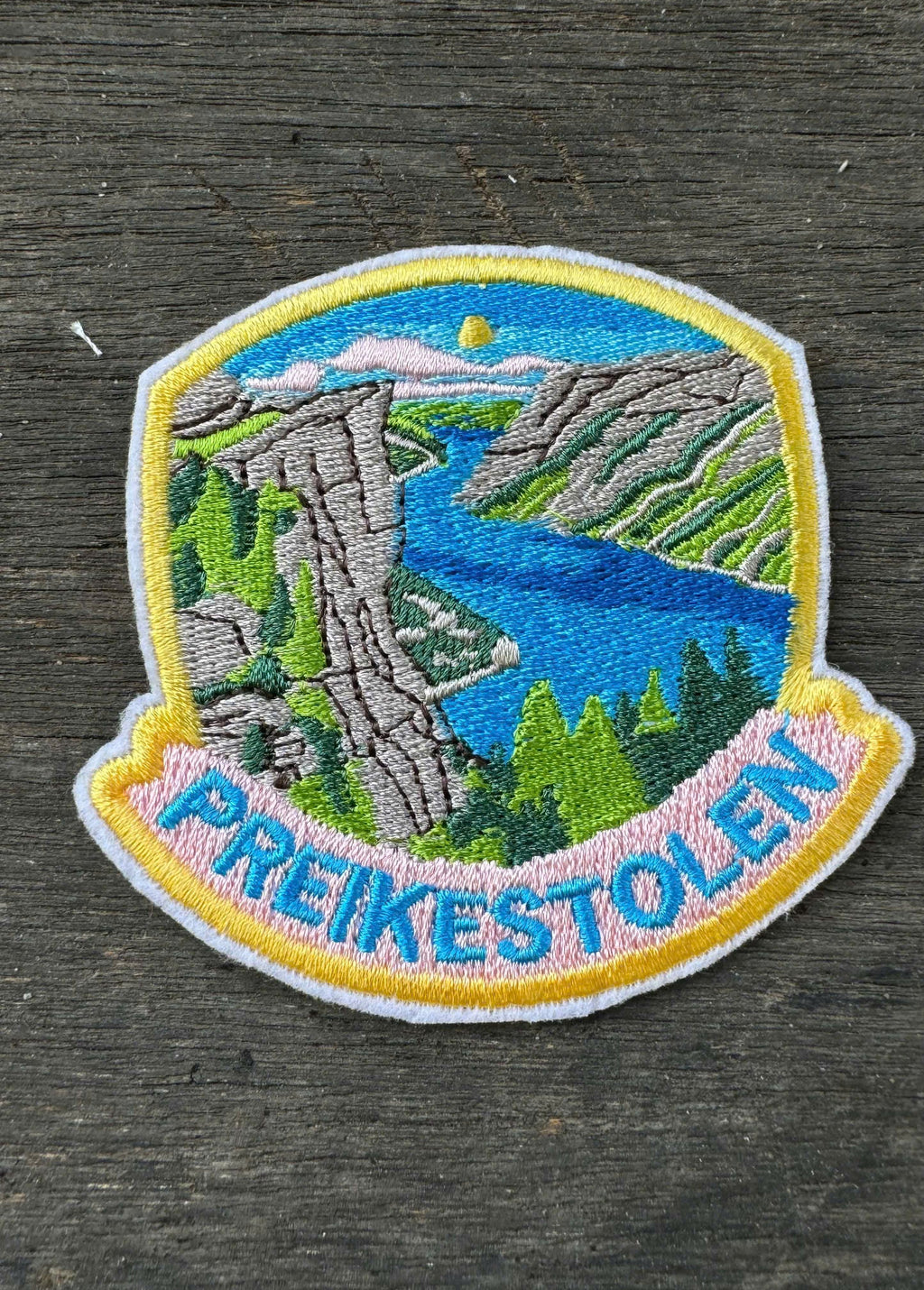 Embroidered patch of Preikestolen with a scenic landscape on a wooden surface