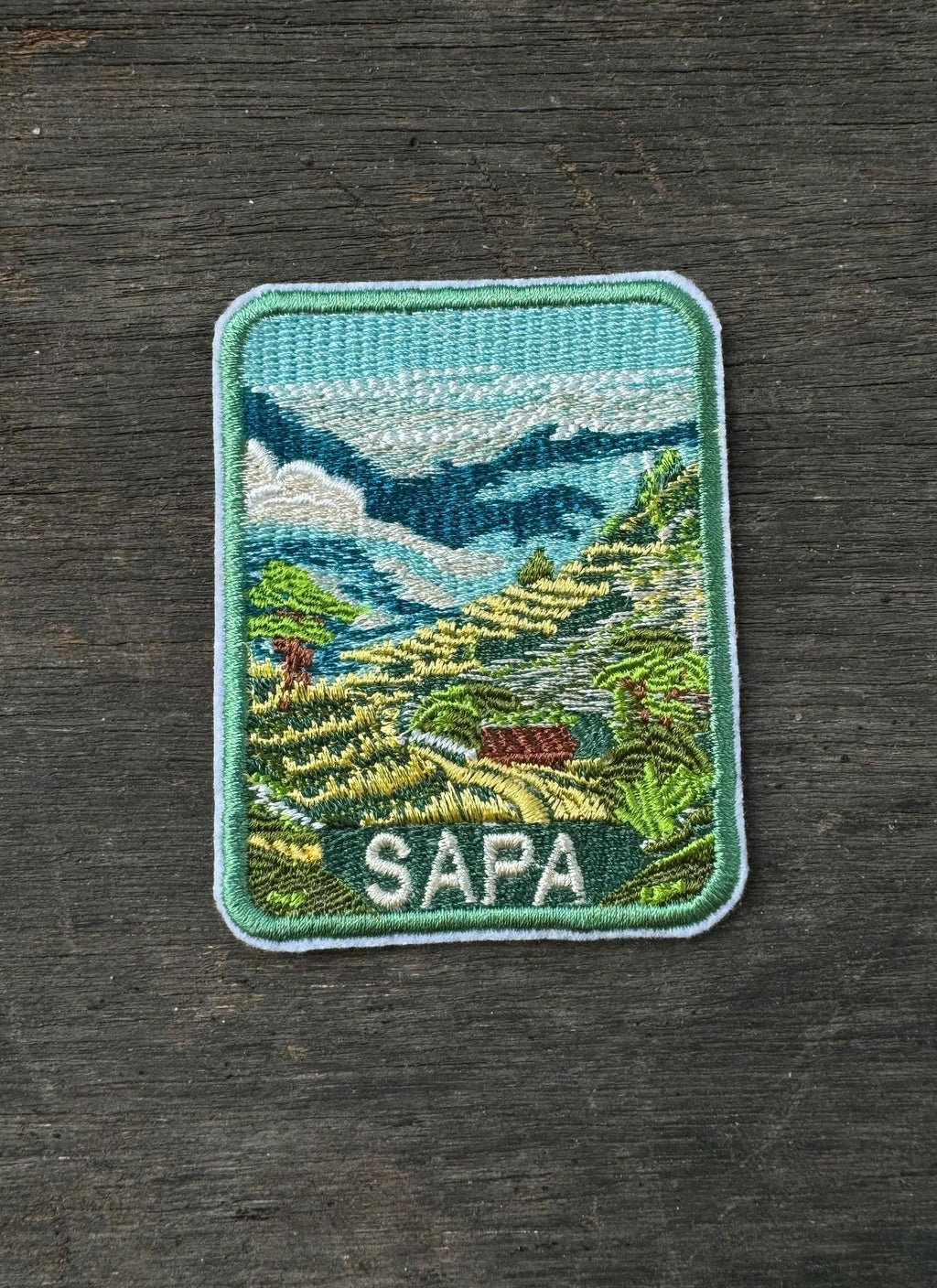 Embroidered patch of Sapa with a scenic design on a dark wooden surface