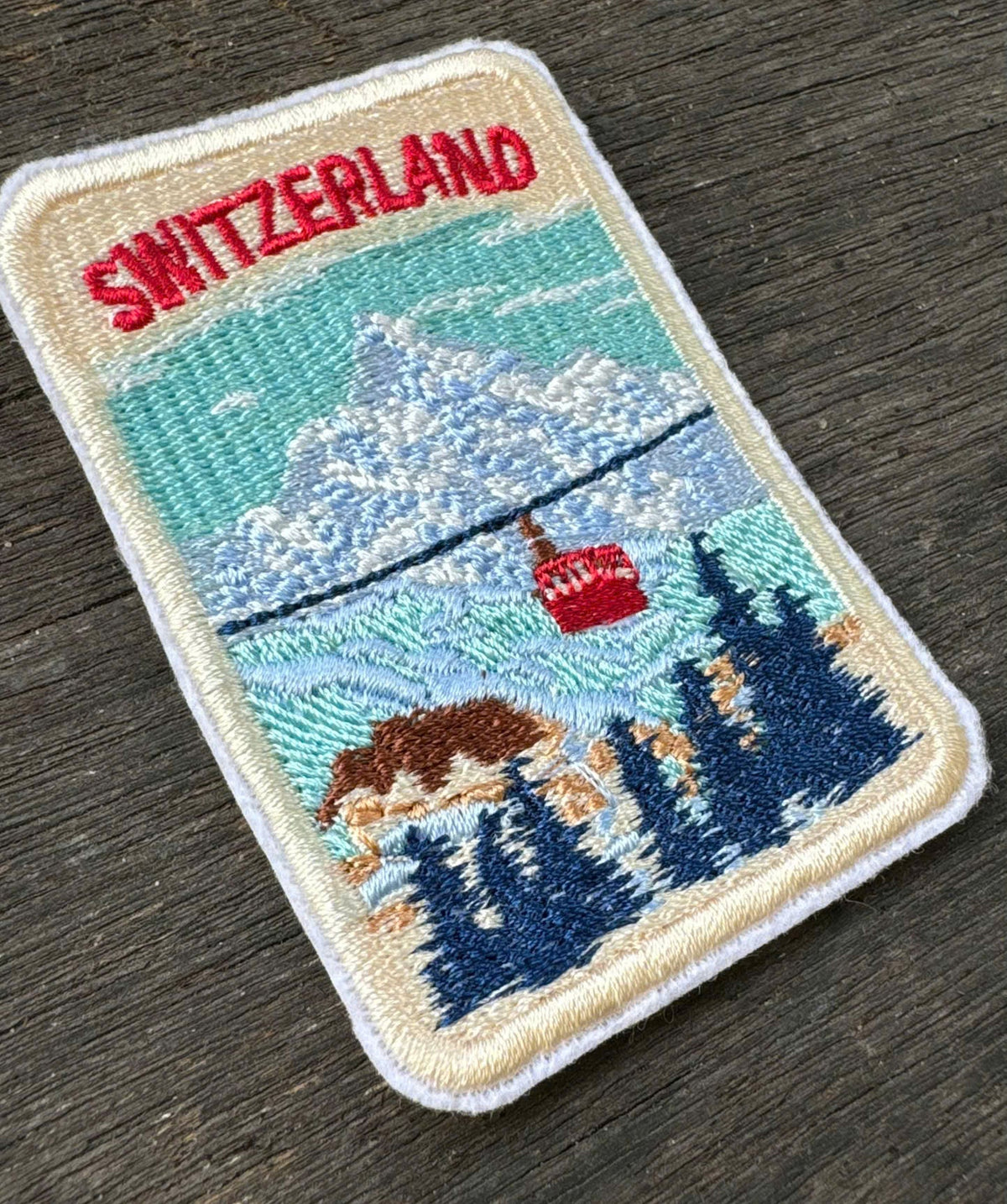 Embroidered patch of Switzerland with a mountain and flag design on a wooden surface