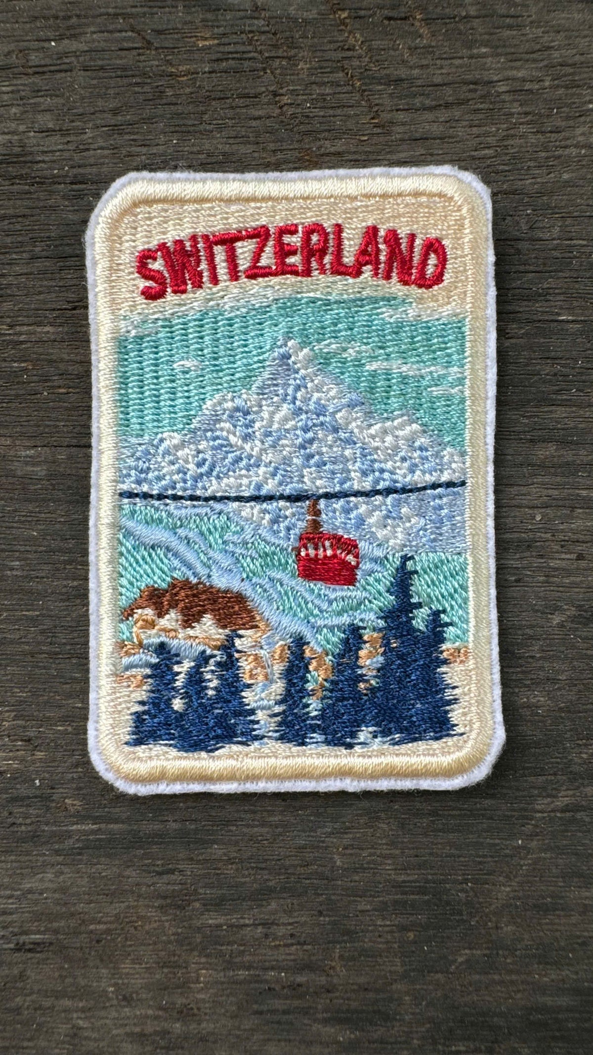 Embroidered patch of Switzerland with mountains and a cable car on a wooden background