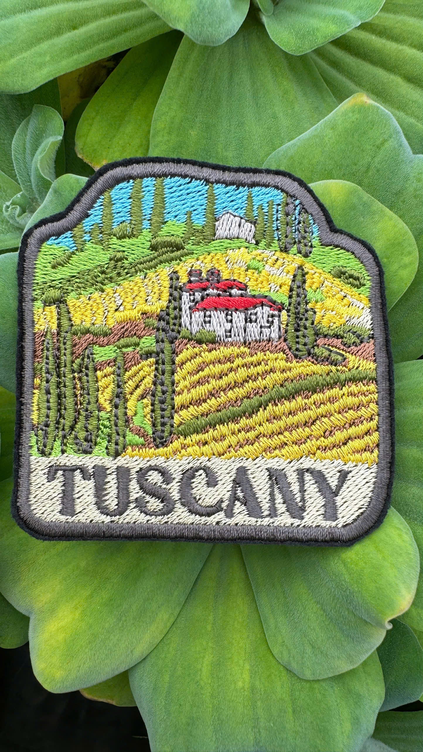 Embroidered patch of Tuscany landscape on green leaves