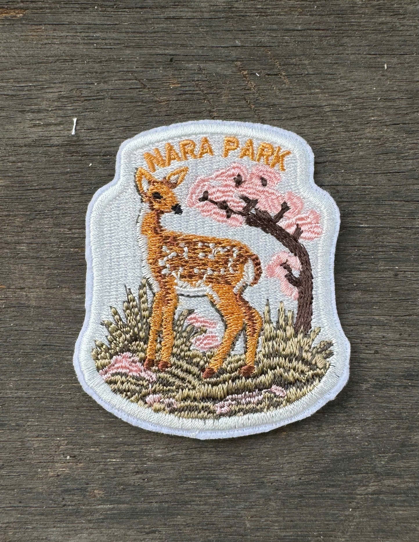 Embroidered patch of a deer and cherry blossom tree with 'Nara Park' text on a wooden surface.