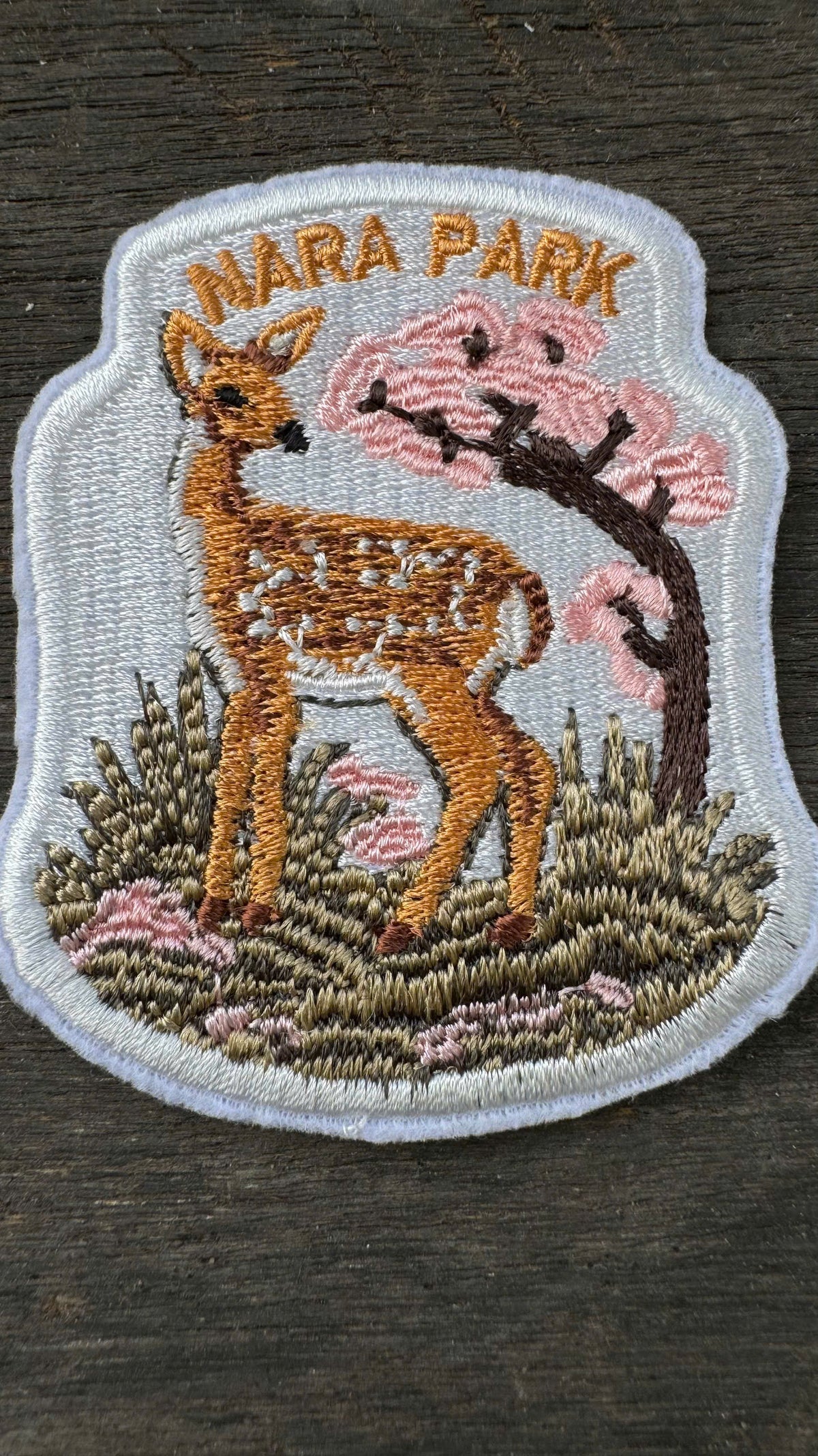 Embroidered patch of a deer and cherry blossoms with 'Nara Park' text on a wooden surface.
