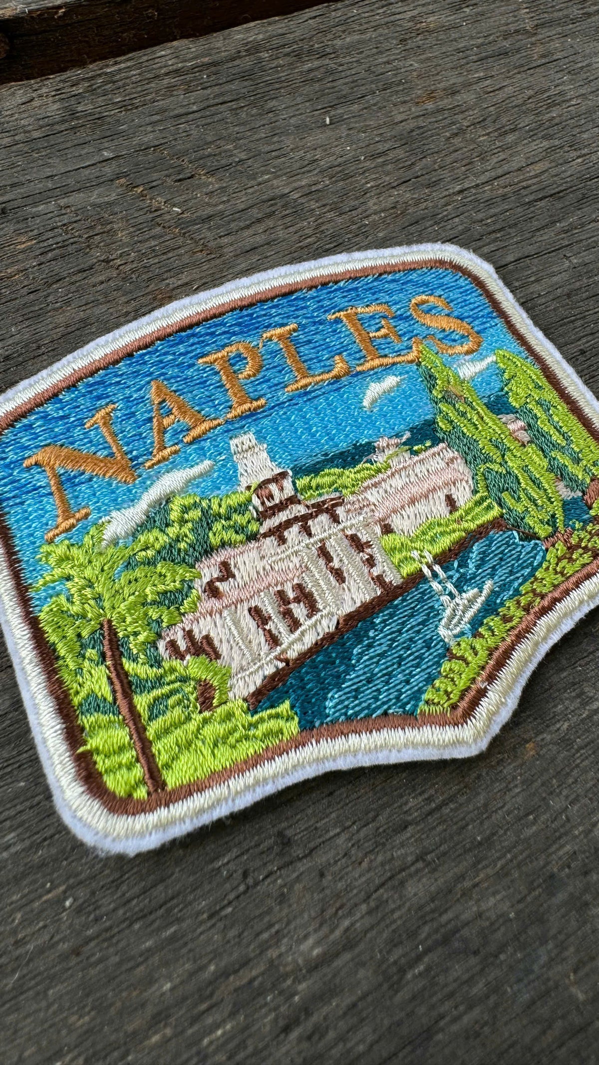 Embroidered patch with 'Naples' text and scenic design on a wooden surface