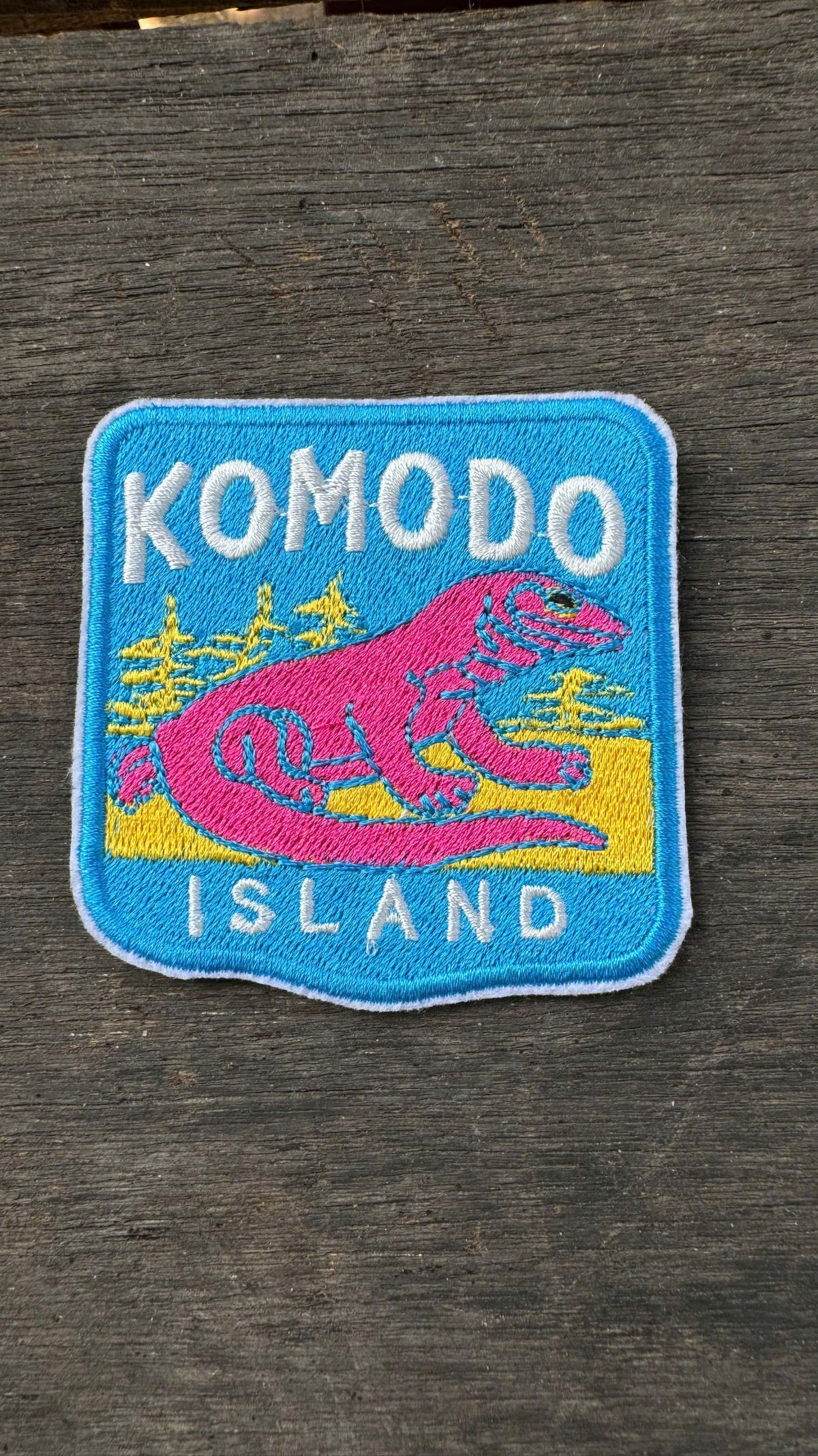 Embroidered patch with a pink Komodo dragon on a wooden surface