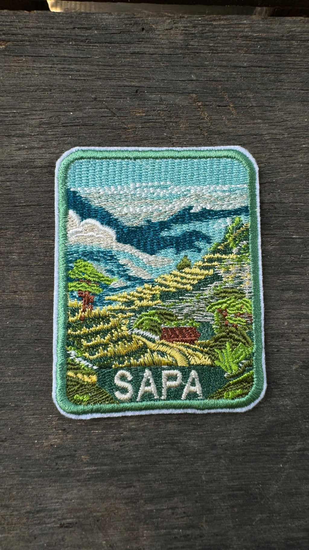 Embroidered patch of Sapa with a scenic landscape on a wooden surface