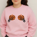 Person wearing a pink sweatshirt with skeleton hand pumpkins design on a plain background