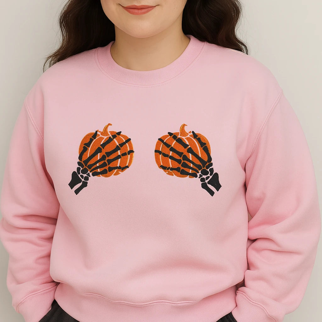 Person wearing a pink sweatshirt with skeleton hand pumpkins design on a plain background