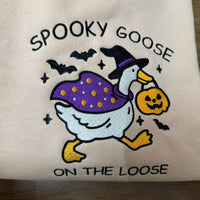 Embroidered design of a goose in a witch costume with 'Spooky Goose on the Loose' text on a beige background.