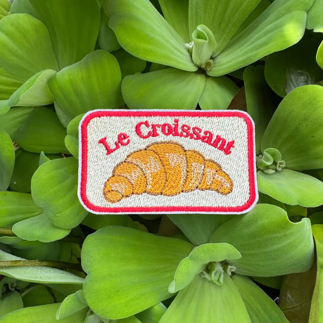 Patch with 'Le Croissant' text and croissant image on green leaves