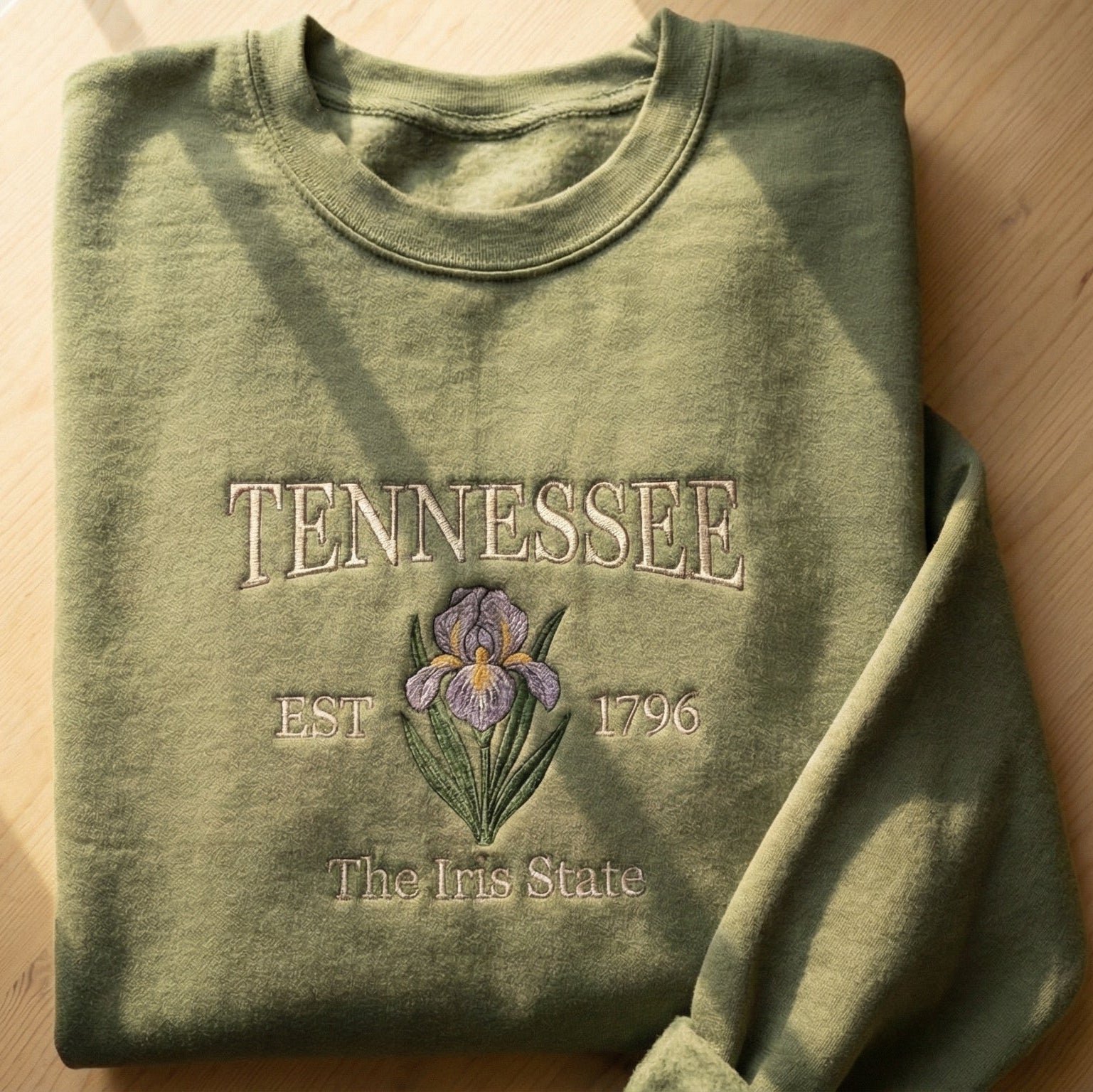 Olive green folded sweatshirt with detailed purple Iris flower embroidery reading Tennessee EST 1796 The Iris State