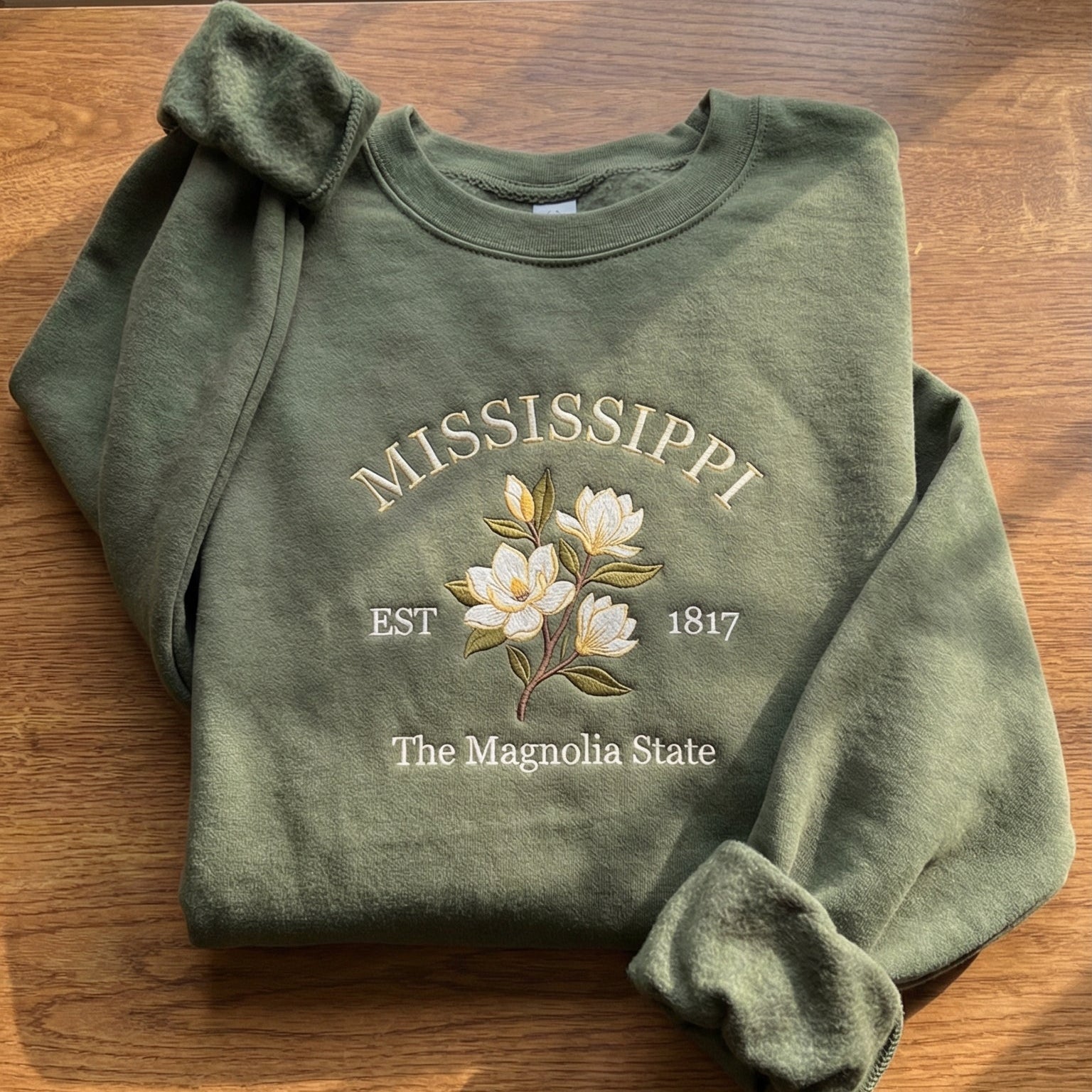 Olive green sweatshirt with detailed white Magnolia flower embroidery reading Mississippi EST 1817 The Magnolia State