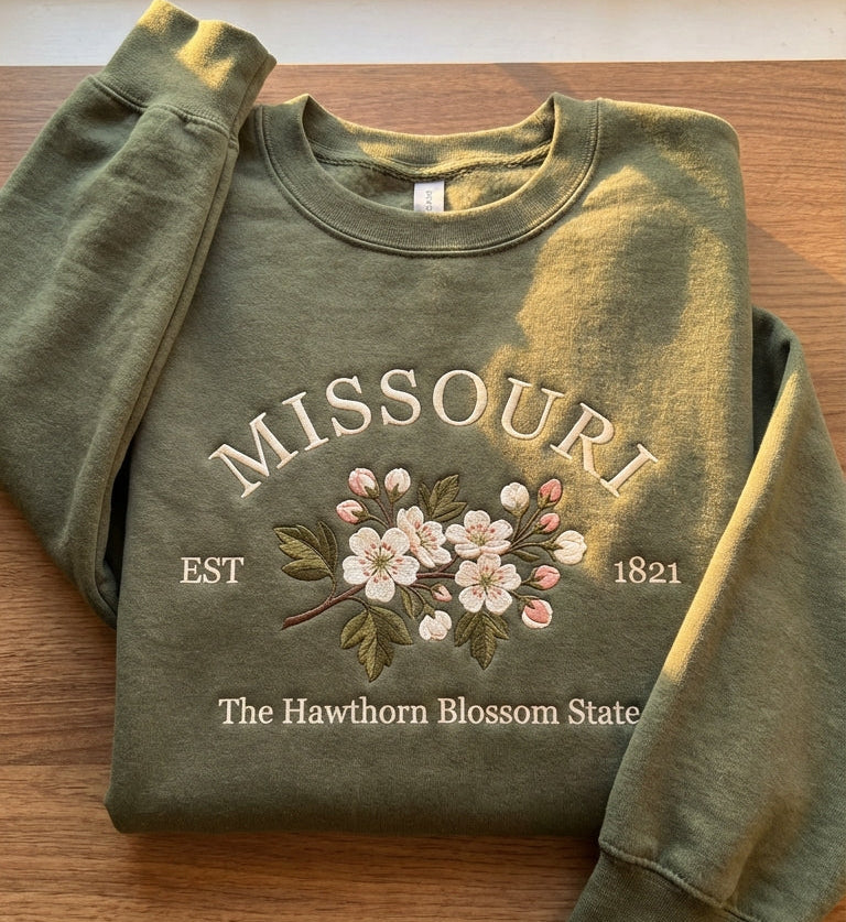 Olive green sweatshirt with detailed white and pink Hawthorn blossom embroidery reading Missouri EST 1821 The Hawthorn Blossom State