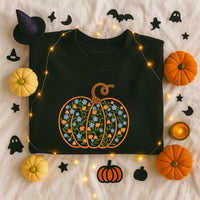 Black sweatshirt with floral pumpkin design surrounded by Halloween decorations on a light background