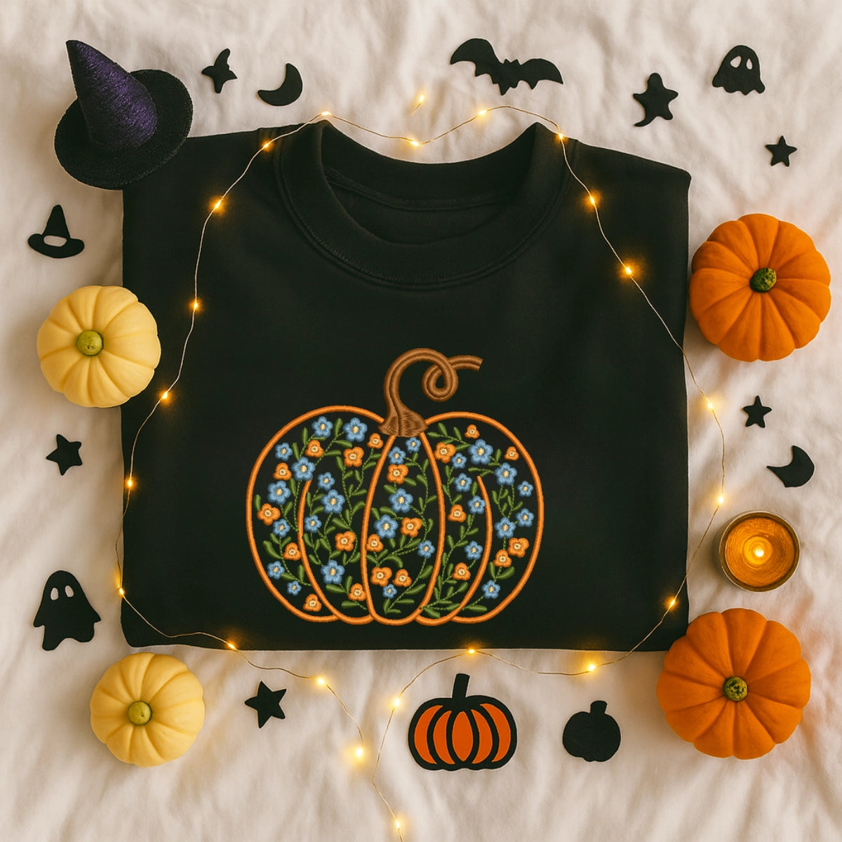 Black sweatshirt with floral pumpkin design surrounded by Halloween decorations on a light background