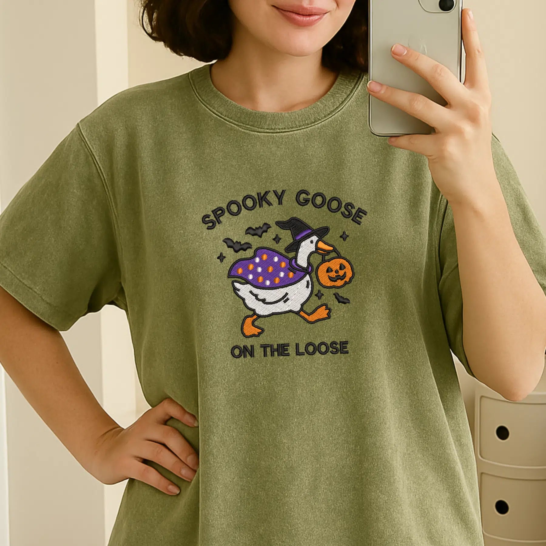 Person wearing a green t-shirt with a Halloween-themed graphic and text.