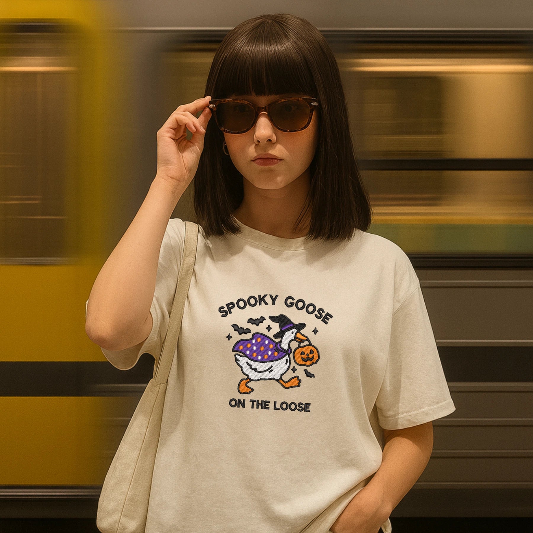Person wearing a t-shirt with 'Spooky Goose' design in front of a blurred train.