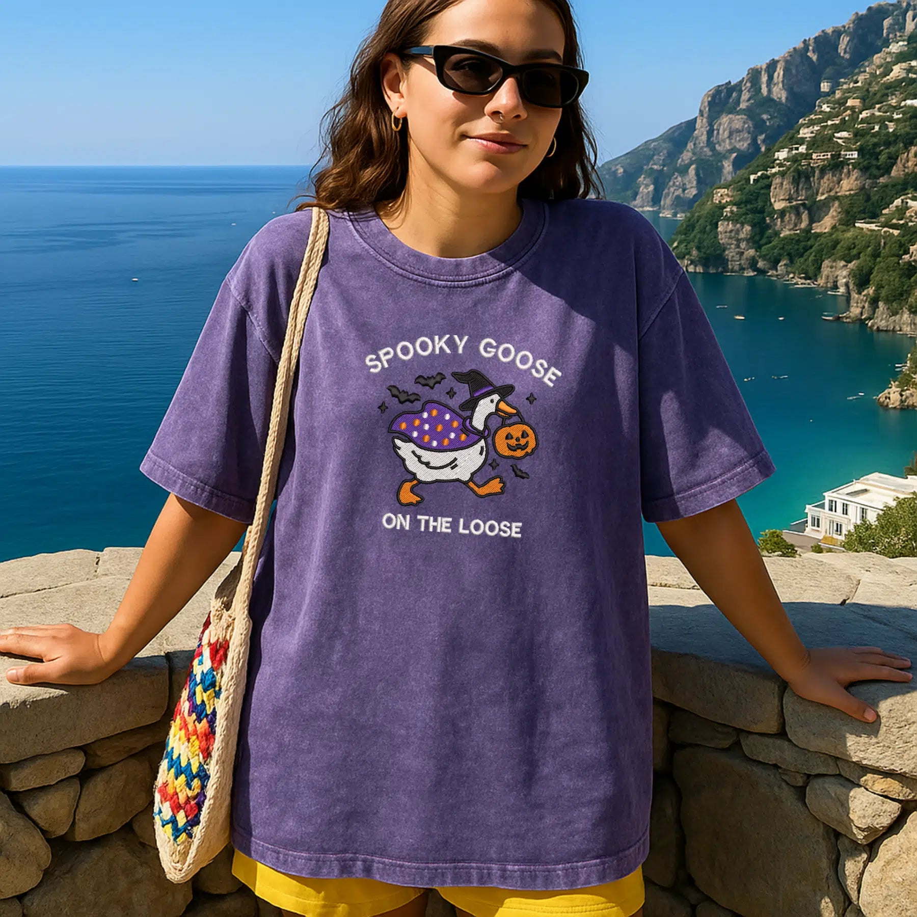 Person wearing a purple t-shirt with a graphic design, standing by a scenic coastal view.