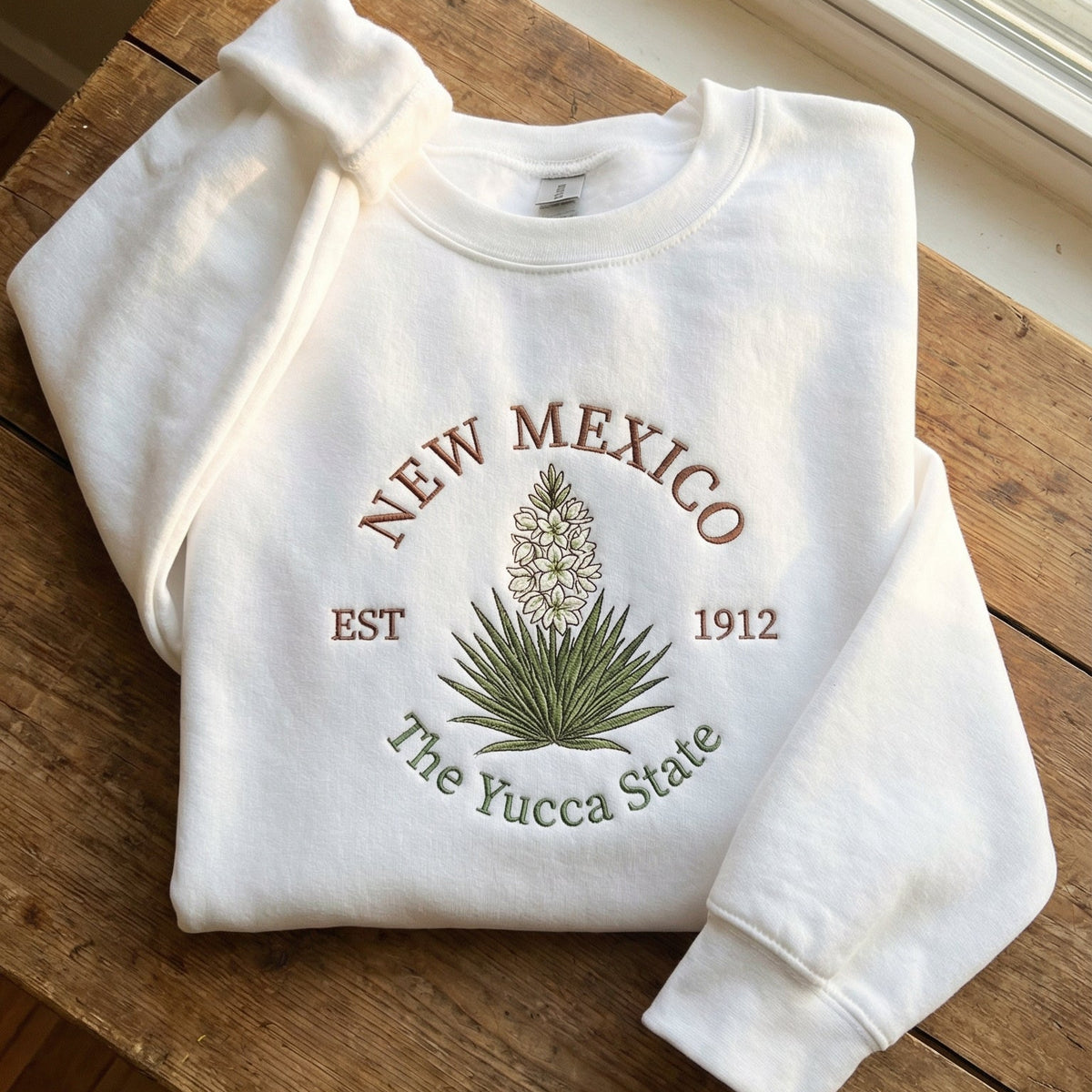 White folded sweatshirt with detailed green Yucca plant and white flower embroidery reading New Mexico EST 1912 The Yucca State