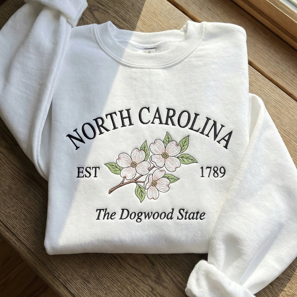 White folded sweatshirt with detailed pink and white Dogwood flower embroidery reading North Carolina EST 1789 The Dogwood State